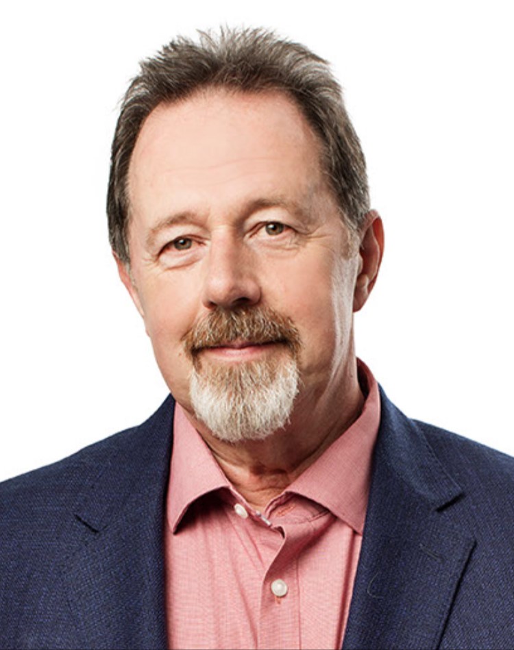 A headshot of a person with short brown hair, brown and white goatee, and wearing a pink collared shirt and navy blue jacket.
