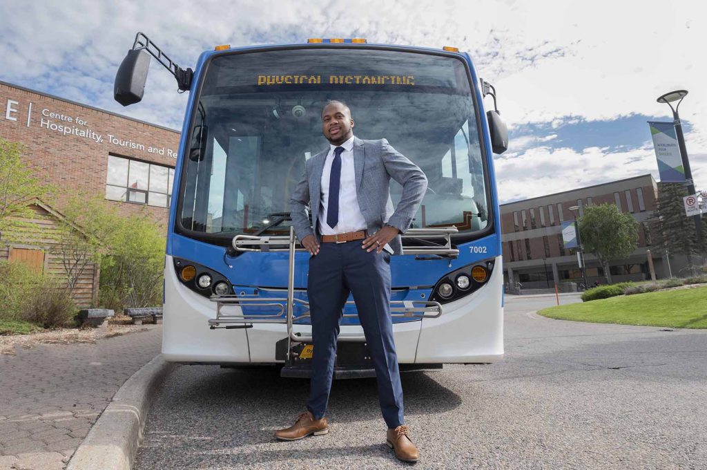 Ronjay Clarke stands in front of a bus with his hands on his hips