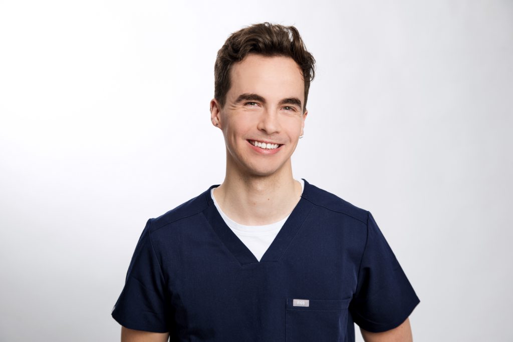 A headshot of a person wearing scrubs smiling at the camera.