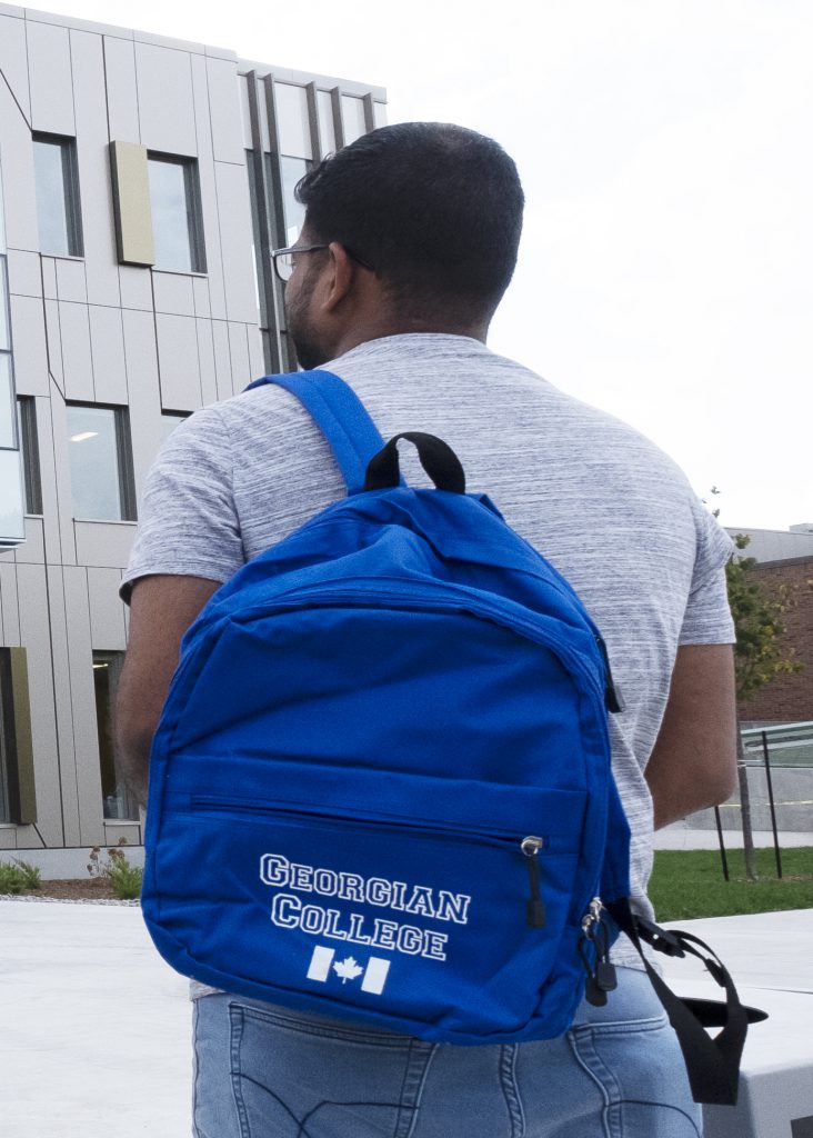 Male student facing a building at the Barrie Campus, Georgian College backpack over his shoulder