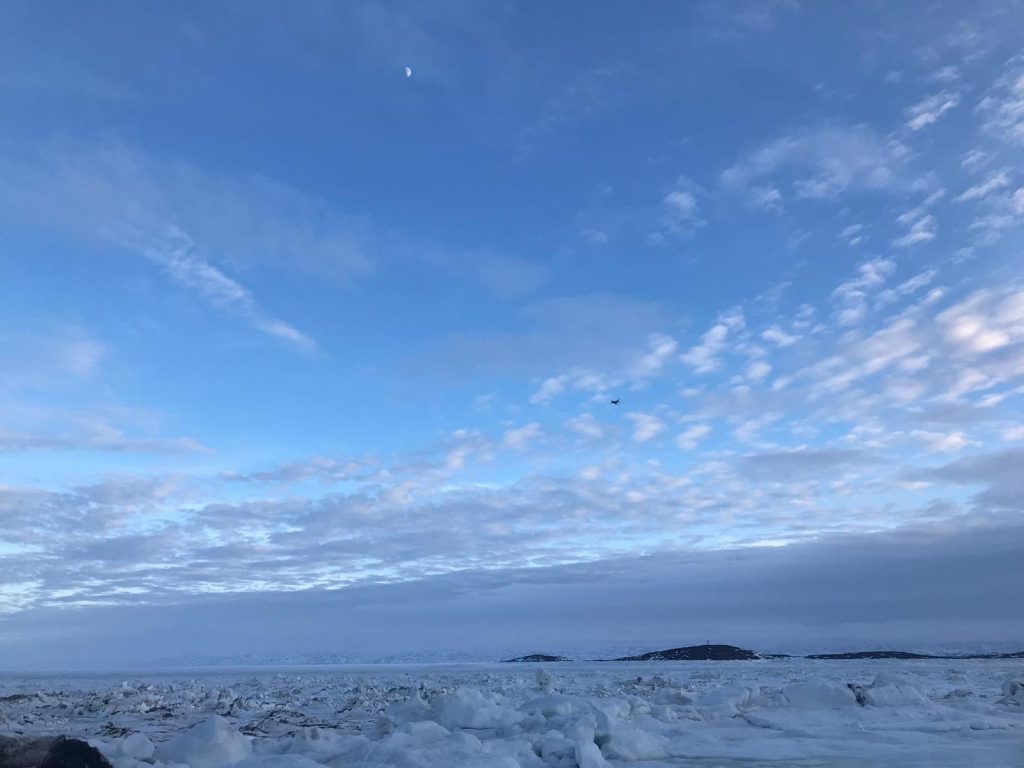 The frozen ocean and a partly cloudy, blue sky in the Canadian arctic.