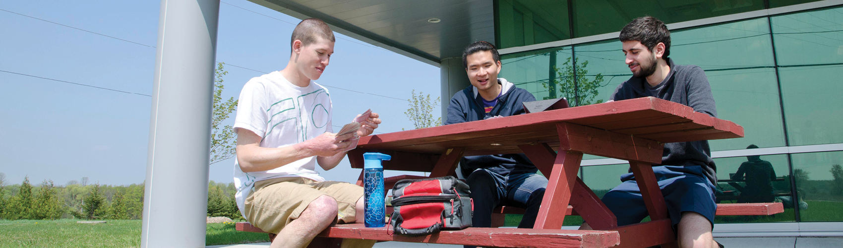 3 male students sitting at a picnic table outside on the South Georgian Bay Campus