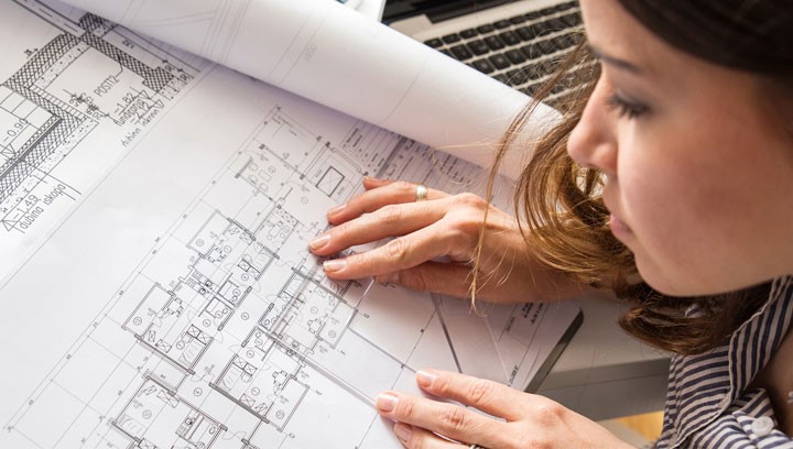 Young-woman-leans-over-house-plans-laid-out-on-desk