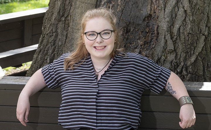 Person smiles at the camera while sitting on a wooden bench in front of a tree