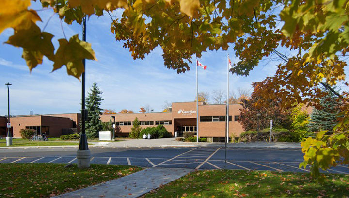 exterior of the Georgian College Orillia campus featuring brick building, trees, flags, streetlights and pavement
