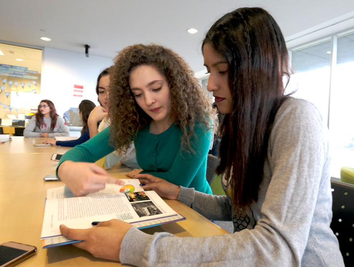 Students sitting at a table looking through a textbook together