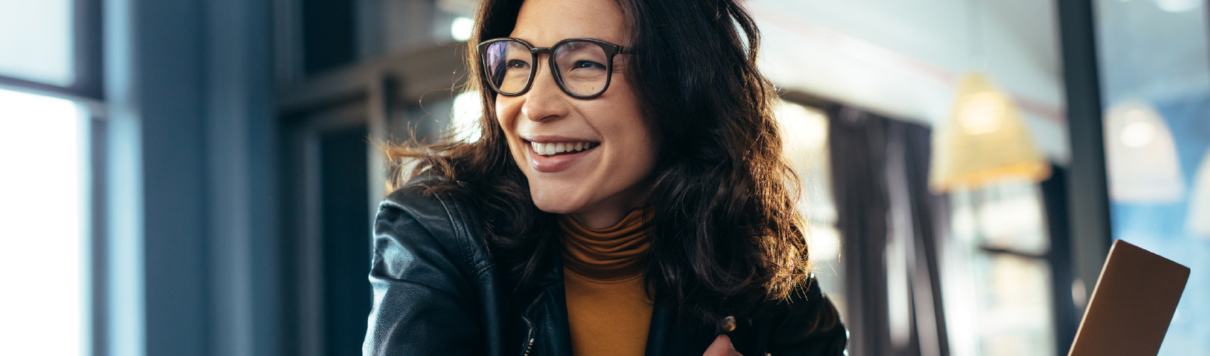 person with brown, curly hear and large-frame glasses looking away from the camera and smiling