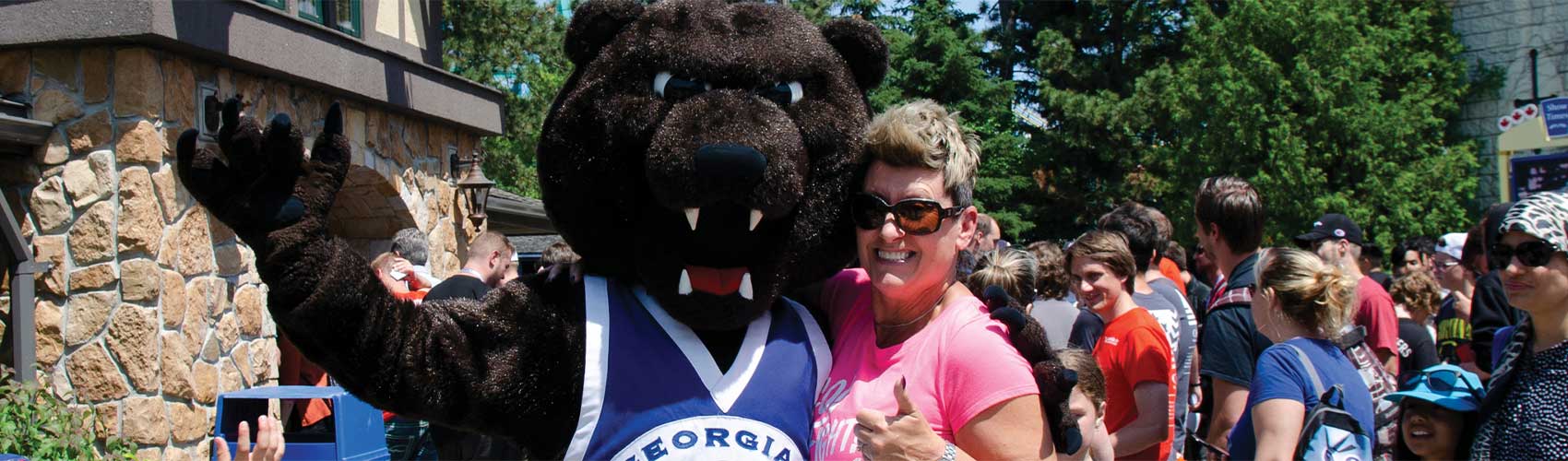 Growler, Georgian's grizzly bear mascot, standing next to an alumni during Georgian Day at Canada's Wonderland