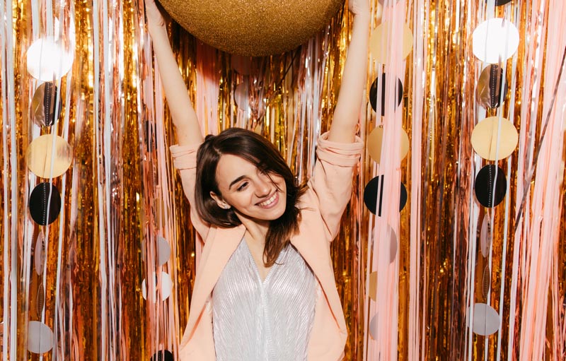woman celebrating by holding her hands above her head in front of tinsel backdrop