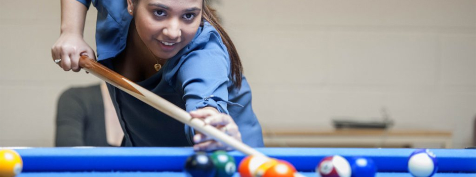 Student leaning over a pool table holding a pool cue during a game of pool inside The Den at Georgian College's Orillia Campus