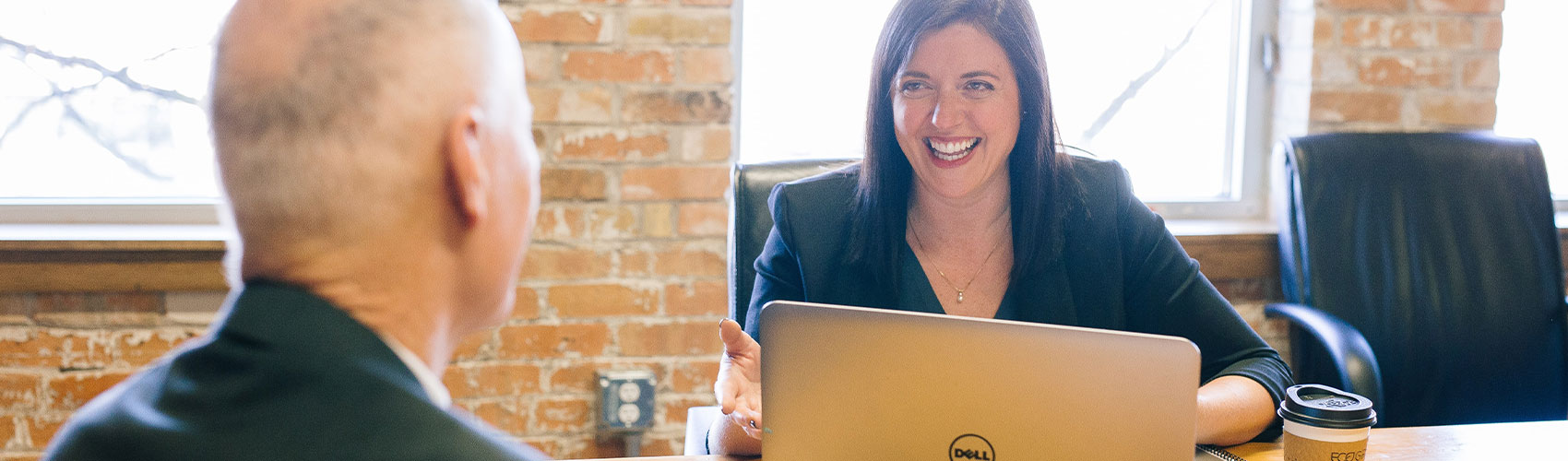A career consultant sitting at a desk with a laptop and coffee cup, while smiling and chatting with an employer connection