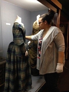 woman wearing a sweater, glasses and latex gloves stands next to museum display case