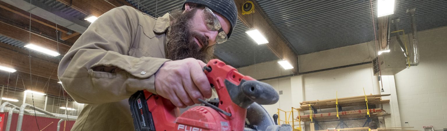 Carpentry and Renovation student wearing a toque and safety glasses while using a circular power saw inside a work shop