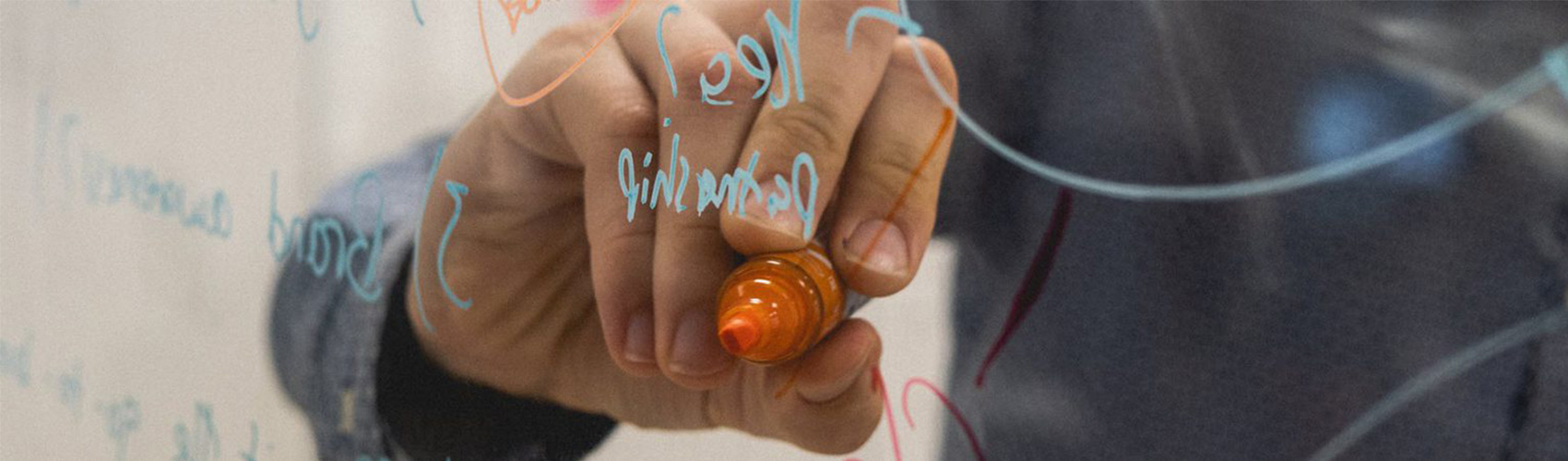 a hand holding an orange whiteboard marker and writing on a glass panel