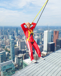 Randy Ugolini teetering on the edge of a high building overlooking the city. He is wearing a safety harness.