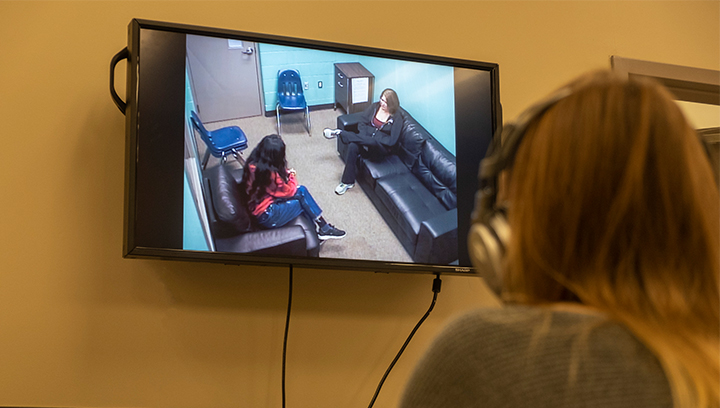 Student with long brown hair wearing a headset while watching a counselling session through a TV screen at Georgian College's Orillia Campus