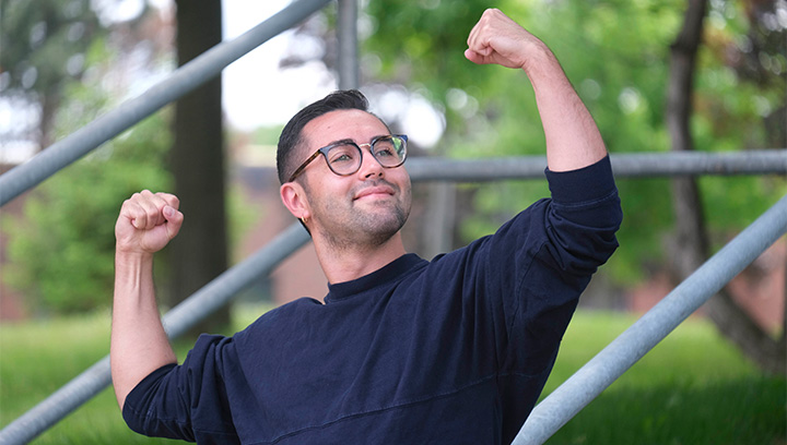 Antonio Sardella wearing glasses and a navy blue shirt with the sleeves rolled up posing with fists in the air