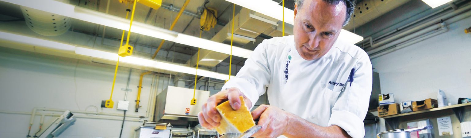 Culinary professor Anthony Borgo wearing a chef's uniform inside the culinary lab grating cheese over a pasta dish