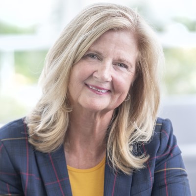 Head shot of Dr. MaryLynn West-Moynes, President and CEO, woman with medium-length blonde hair, wearing navy red and yellow striped jacket, yellow t-shirt, warm smile