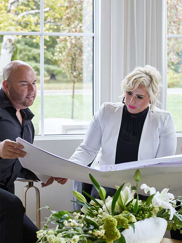 Two people sitting and looking at a large piece of paperwork in front of white flowers