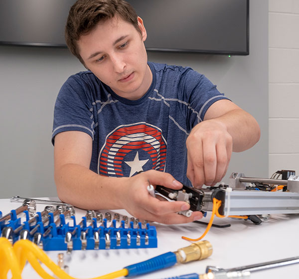 A young white male wearing a t-shirt working on some equipment at a table