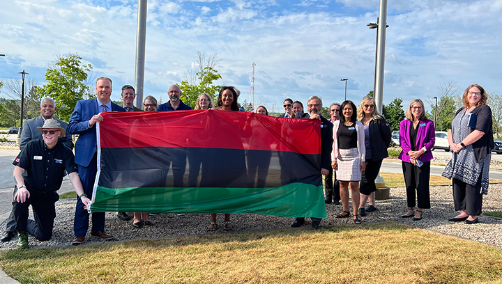 A group of Georgian employees holding a large Pan-African flag in front of the Owen Sound Campus Cenotaph prior to the flag raising for Emancipation Day 2022