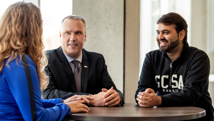 Kevin Weaver, Georgian College's President and CEO, in a suit and tie sitting at a table with Ishaan Sachdeva, President, GCSA Barrie and a student