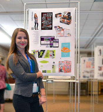 graphic design student standing next to a poster board featuring her work