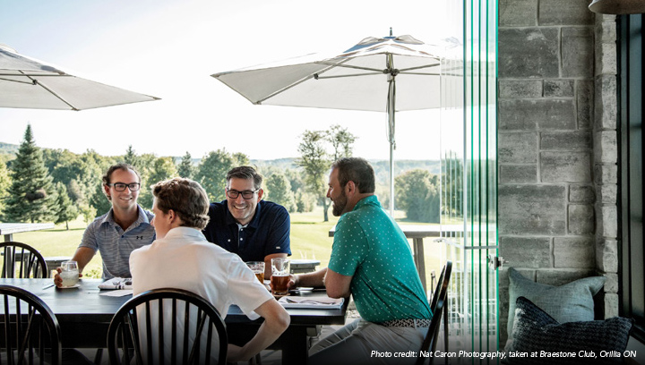 A group of four people sitting at a table overlooking a golf course at Braestone Club in Orillia