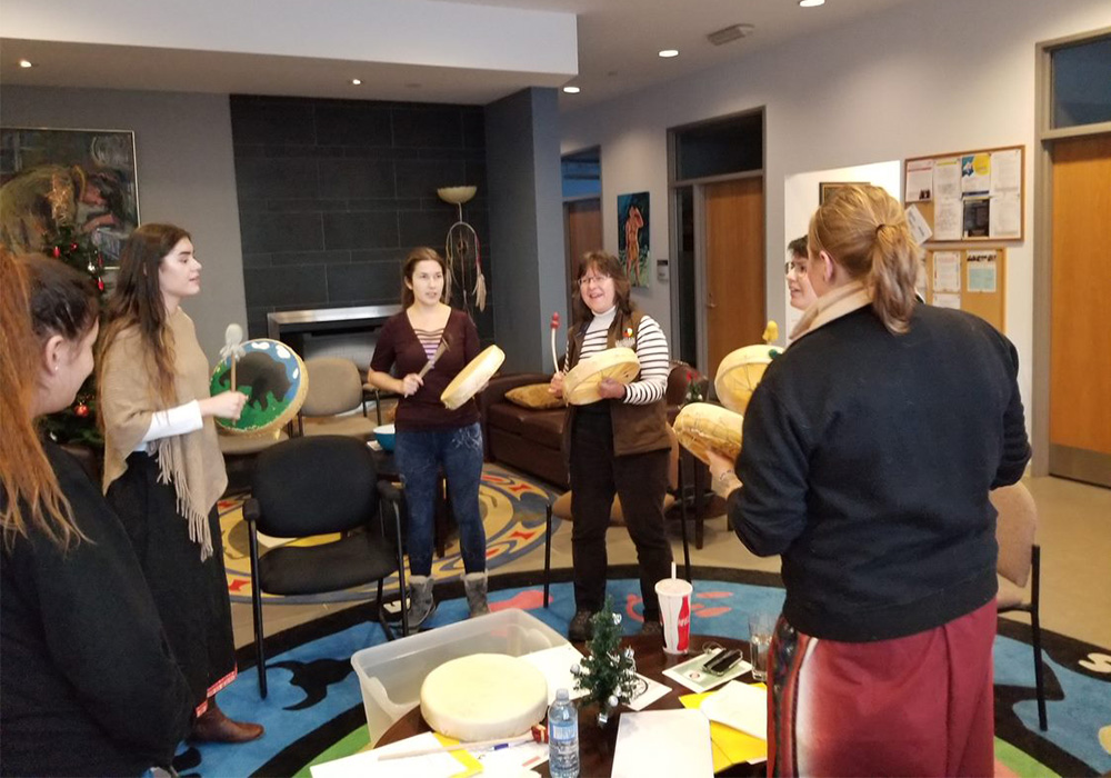 a group of women standing and using handmade drums at a drum making night held in the Wiidookdaading Indigenous Resource Centre