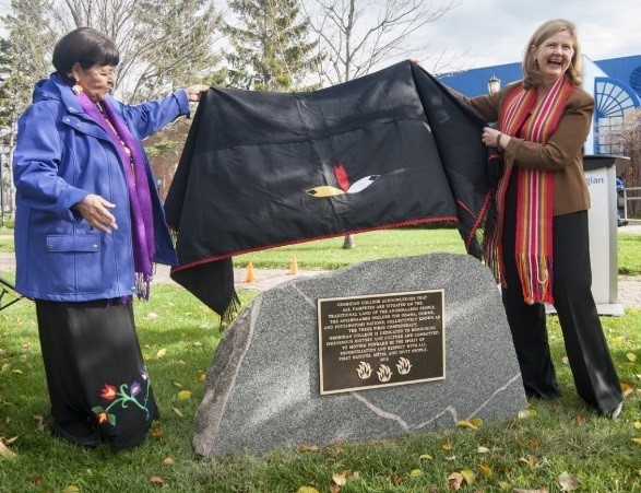 Elder Lorraine McRae and President and CEO MaryLynn West-Moynes unveil the Land Acknowledgment plaque on a stone outside at the Barrie Campus