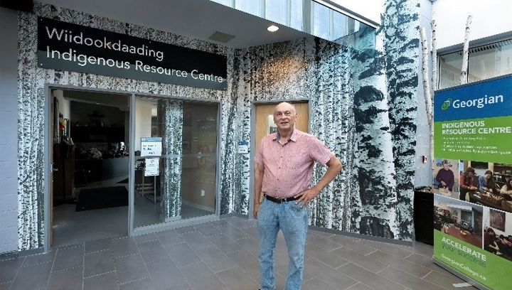 Greg McGregor stands in front of the new mural and sign welcoming people to the Windookdaading Indigenous Resource Centre at the Barrie campus