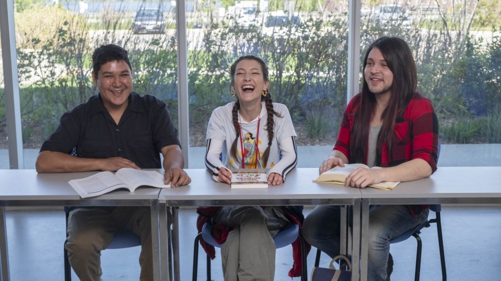 three Indigenous students sitting together at a table with books in front of them