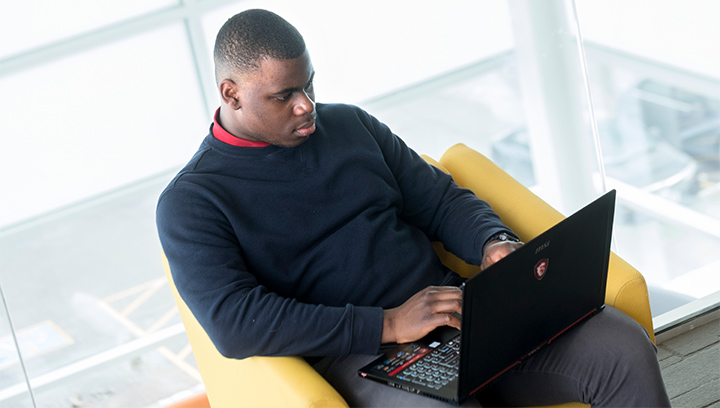 male student sitting on a yellow lounge chair using a laptop computer
