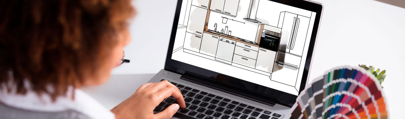 Kitchen and Bath Designer sitting at a desk using AutoCAD software on a laptop and colour swatches to design a kitchen remodel