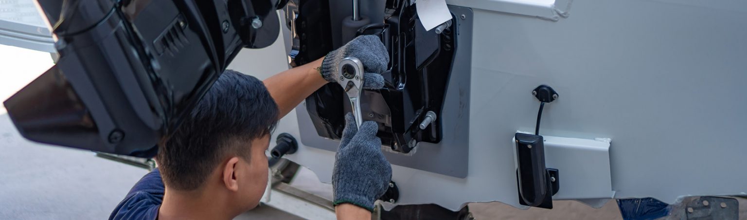 A Marine Engine Mechanic wearing gloves and using a ratcheting socket wrench to repair the motor attachment on a boat
