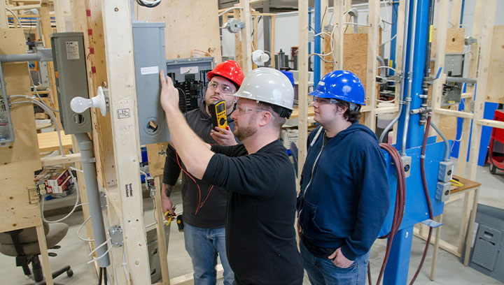 Three people wearing hard hats working on an electrical panel