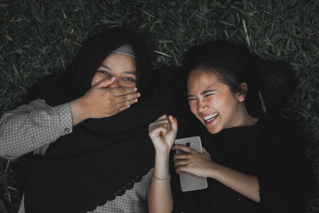 2 females lying in the grass laughing