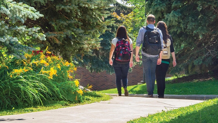 three Georgian students walking on a paved pathway surrounded by trees and flowers at the Barrie Campus