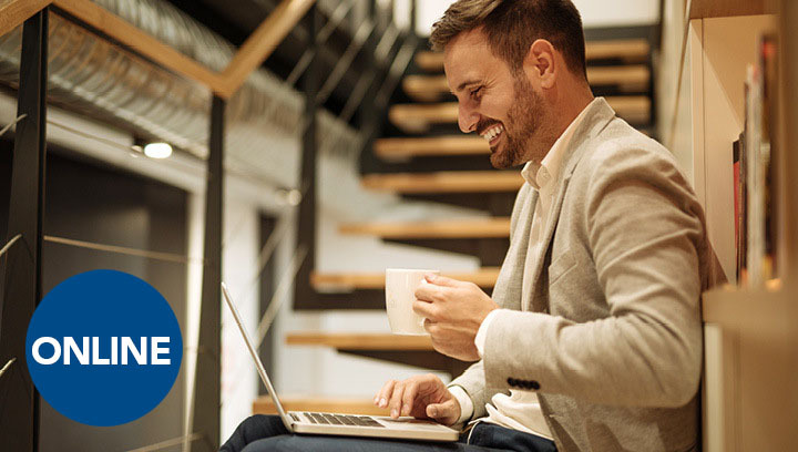a business professional sitting on a staircase using a laptop and holding a mug while smiling