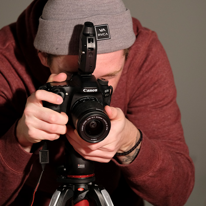 A student in a burnt orange sweatshirt and taupe RVCA had holding and looking into a Canon digital camera on a tripod