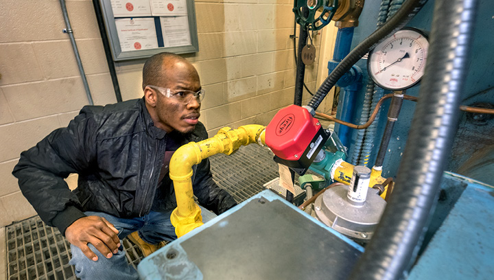 A Plumbing Techniques student wearing safety glasses and crouching while inspecting a piece of equipment