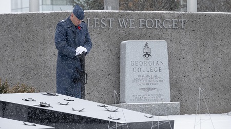 Member of Honour Guard in blue military uniform stands at Georgian Cenotaph in snow, head down