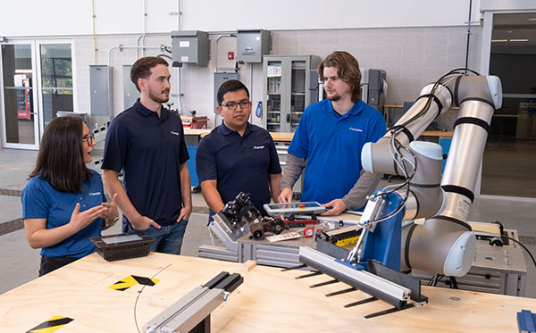 Four young people standing in front of a table with robotic equipment on it.