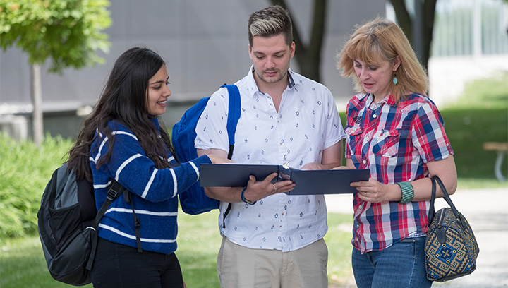 Three people standing outside on a sunny summer day holding and looking down at a binder