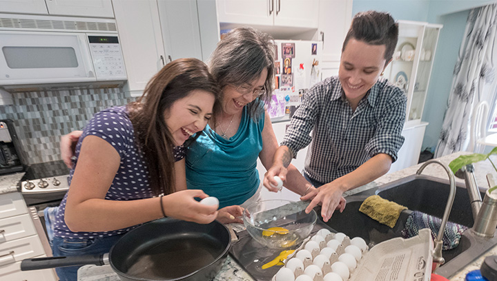 two international students in the kitchen with their homestay host cracking eggs