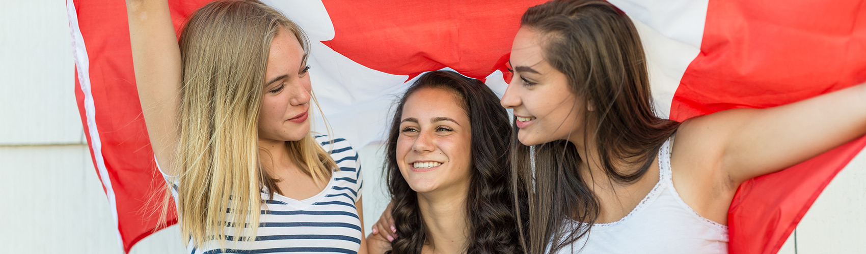 Three female students holding a large Canadian flag over their shoulders
