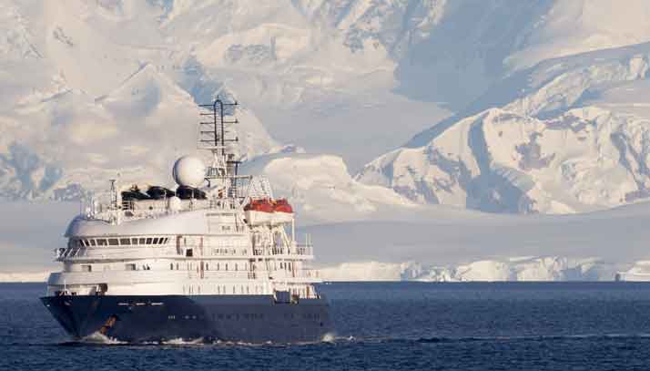 Commercial ship sailing away from snow covered arctic coastline
