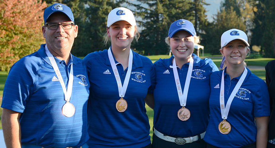 three women and one man wearing blue Georgian golf shirts and a medal around their necks standing on a golf course